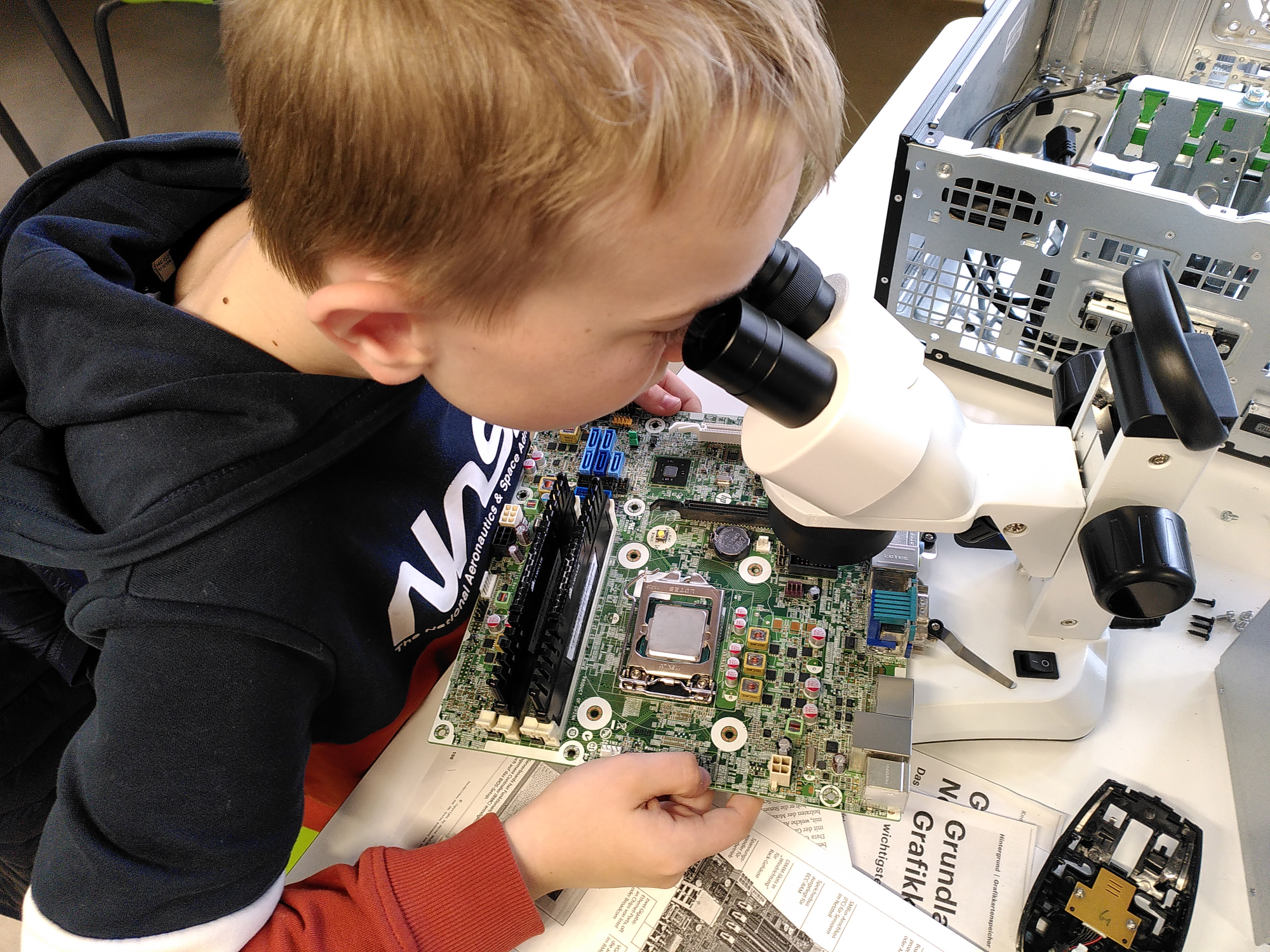 Mit einer Stereolupe unter­such­t ein Schüler die ver­schiedenen Computer-Bauteile.